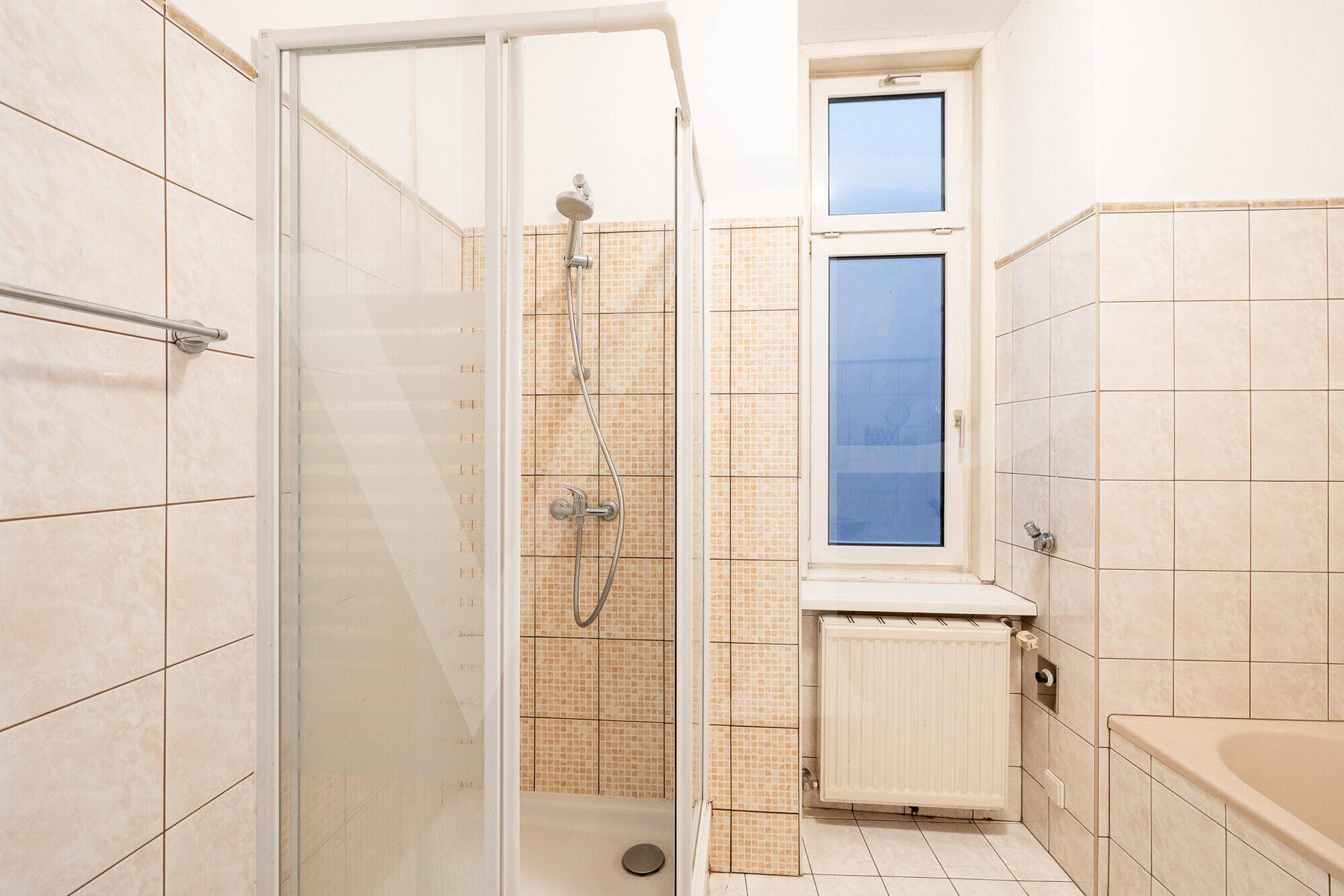 Badezimmer mit Duschkabine, beigefarbenen Fliesen und einem Fenster.