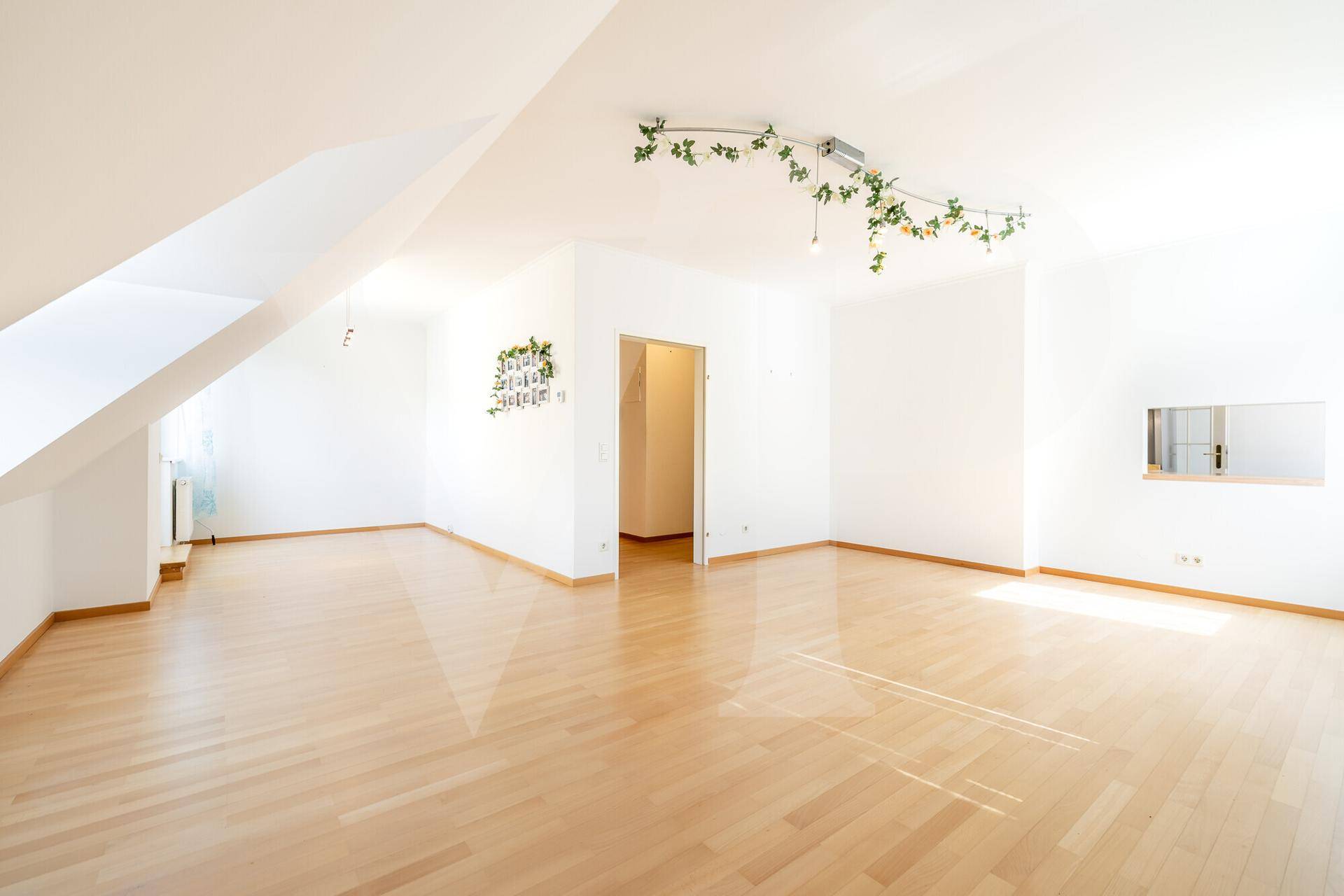 Geräumiger, leerer Raum im Dachgeschoss mit hellem Holzparkett und schrägen Decken.
