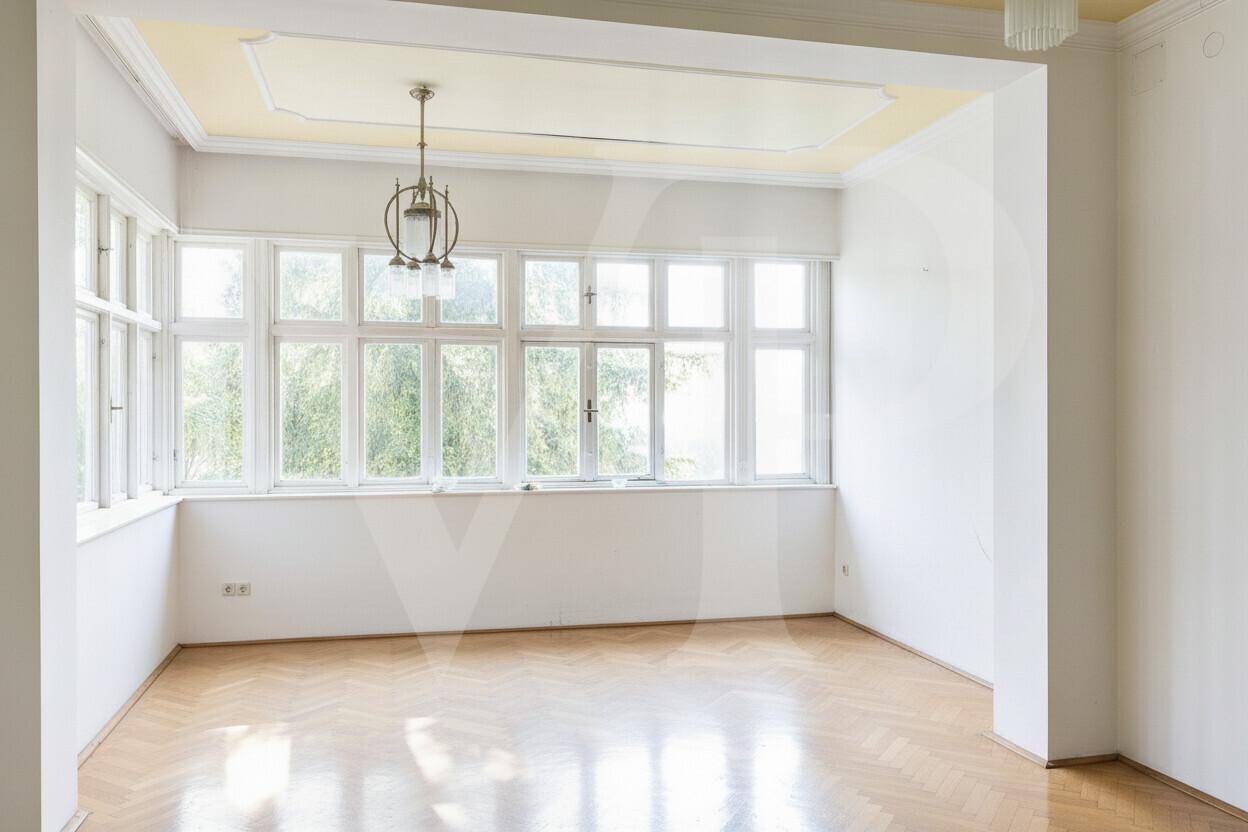 Helles, leeres Zimmer mit Fischgrätparkett, großen Fenstern und einer Stuckdecke.