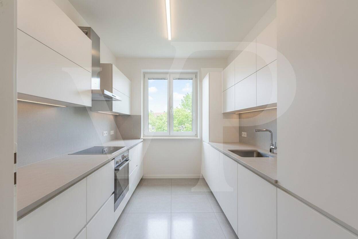 Moderne weiße Küche mit Einbaugeräten, viel Stauraum und Fenster.