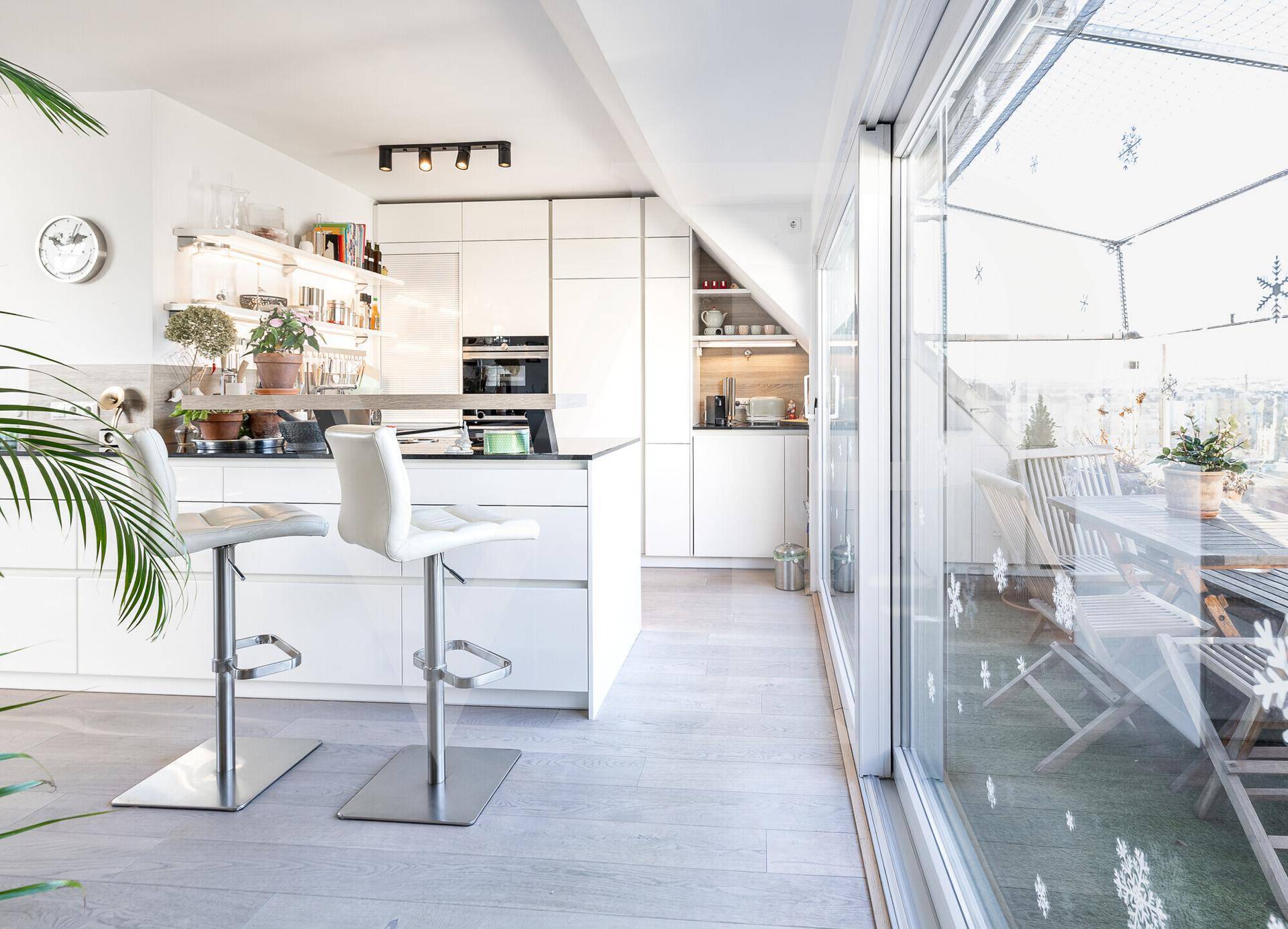 Moderne weiße Küche mit Kochinsel und Zugang zur sonnigen Dachterrasse.