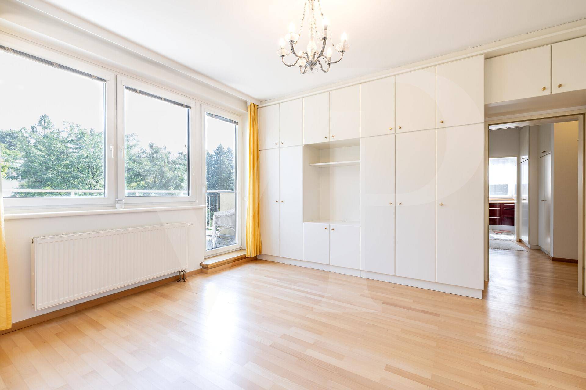 Geräumiger Raum mit Einbauschränken, Holzfußboden und Balkonzugang, ideal als Schlaf- oder Wohnzimmer.