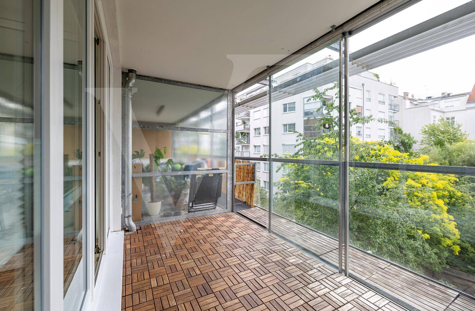 Helle, verglaste Loggia mit Holzboden und Blick auf die umliegenden Gebäude und Bäume.