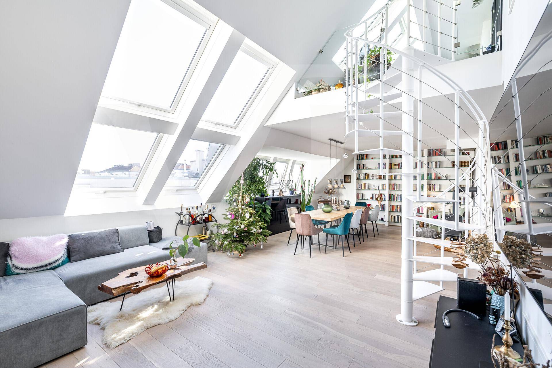 Lichtdurchfluteter Wohn-Essbereich eines Penthouses mit hohen Decken, großen Dachfenstern und einer eleganten Wendeltreppe.