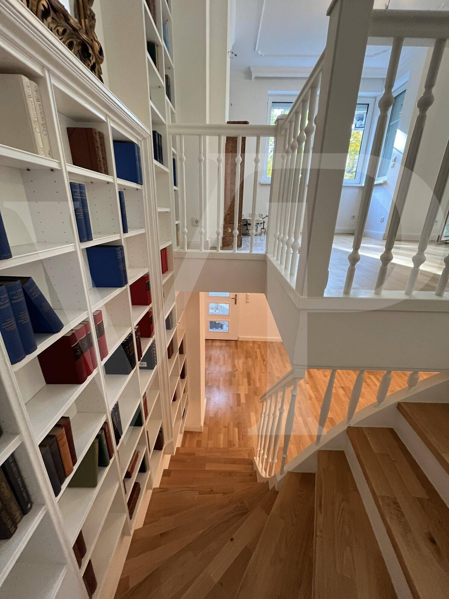 Treppenaufgang mit Holzstufen und Bücherregalen, verbindet die Wohnebenen.