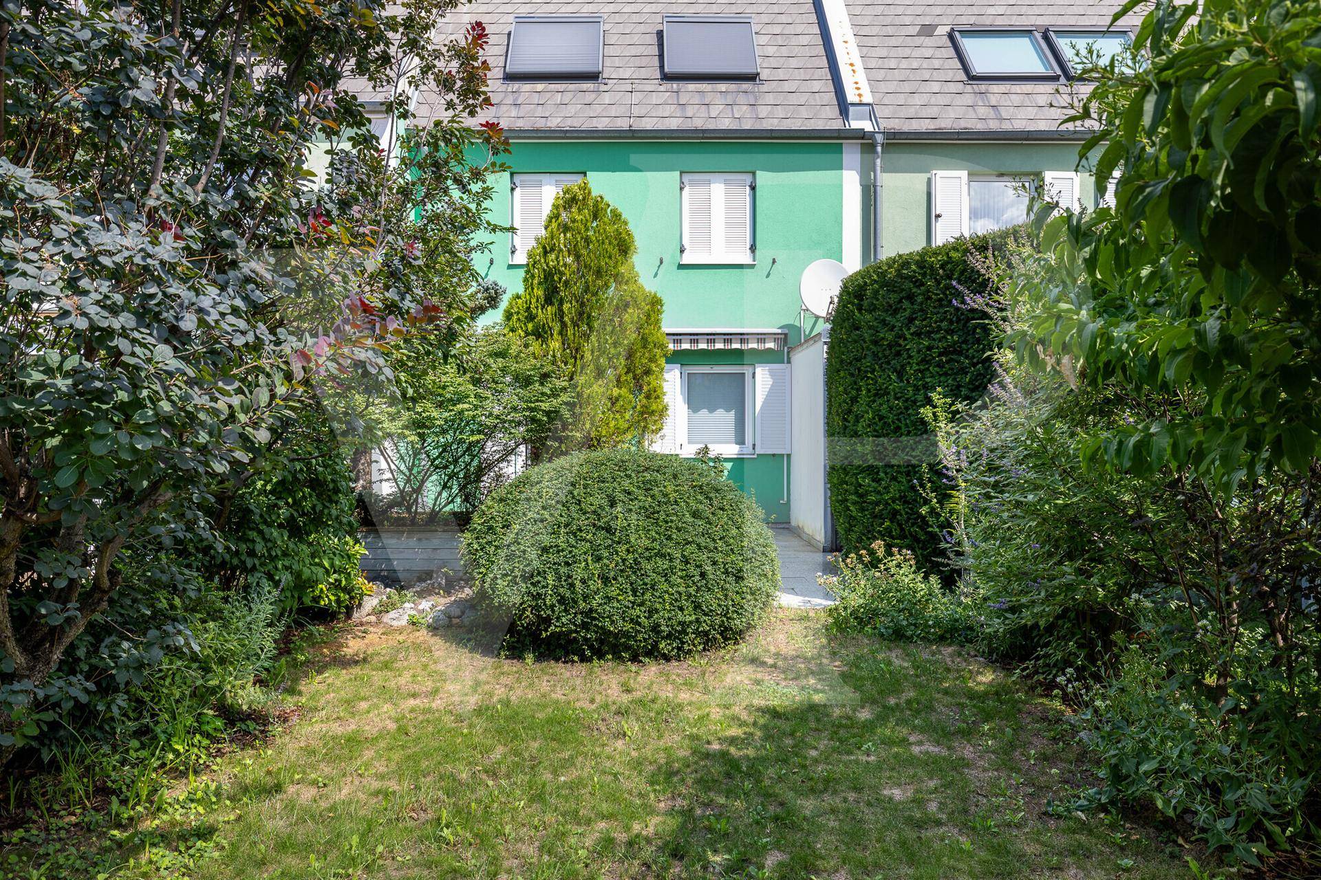 Gepflegter Garten hinter dem Reihenhaus mit Rasenfläche und verschiedenen Sträuchern.