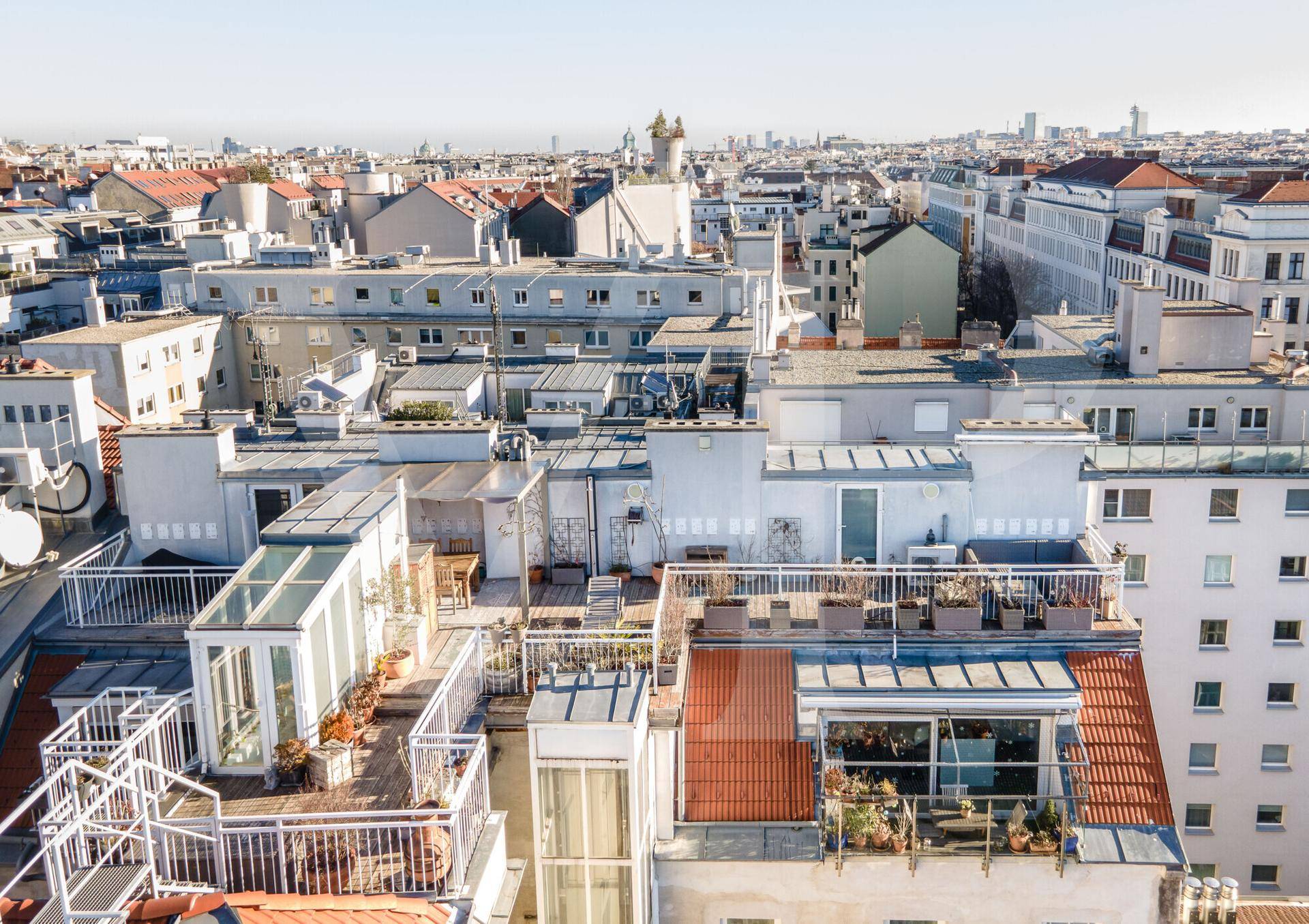 Luftaufnahme der Dächer mit mehreren Terrassen und Blick über die Stadt.