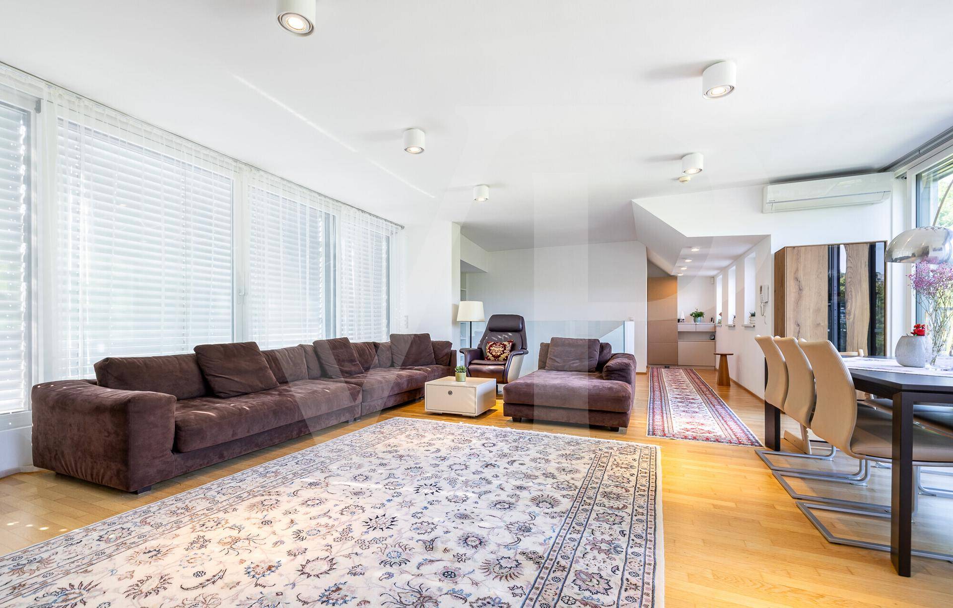 Weitläufiger Wohnbereich mit großem Sofa, Holzboden und breiten Fenstern für viel Tageslicht.