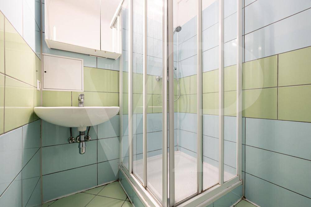 Badezimmer mit Duschkabine, Waschbecken und farbigen Fliesen.