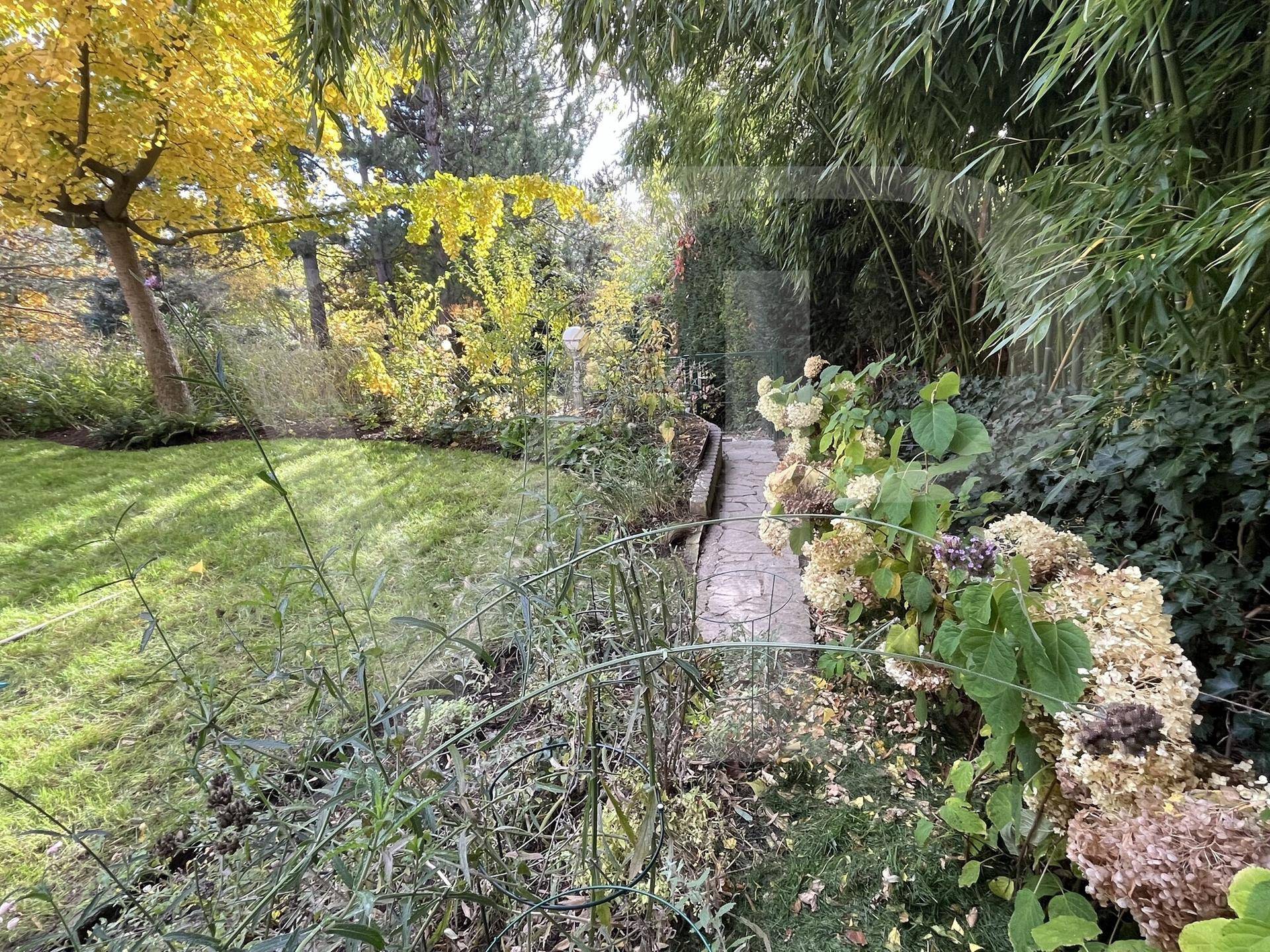 Verwunschener Gartenweg aus Steinplatten, umgeben von dichter Vegetation und Bäumen.
