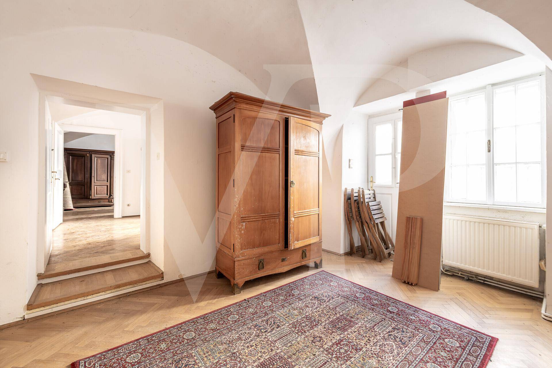 Helles Zimmer mit Gewölbedecke, Fischgrätparkett und einem antiken Holzschrank.