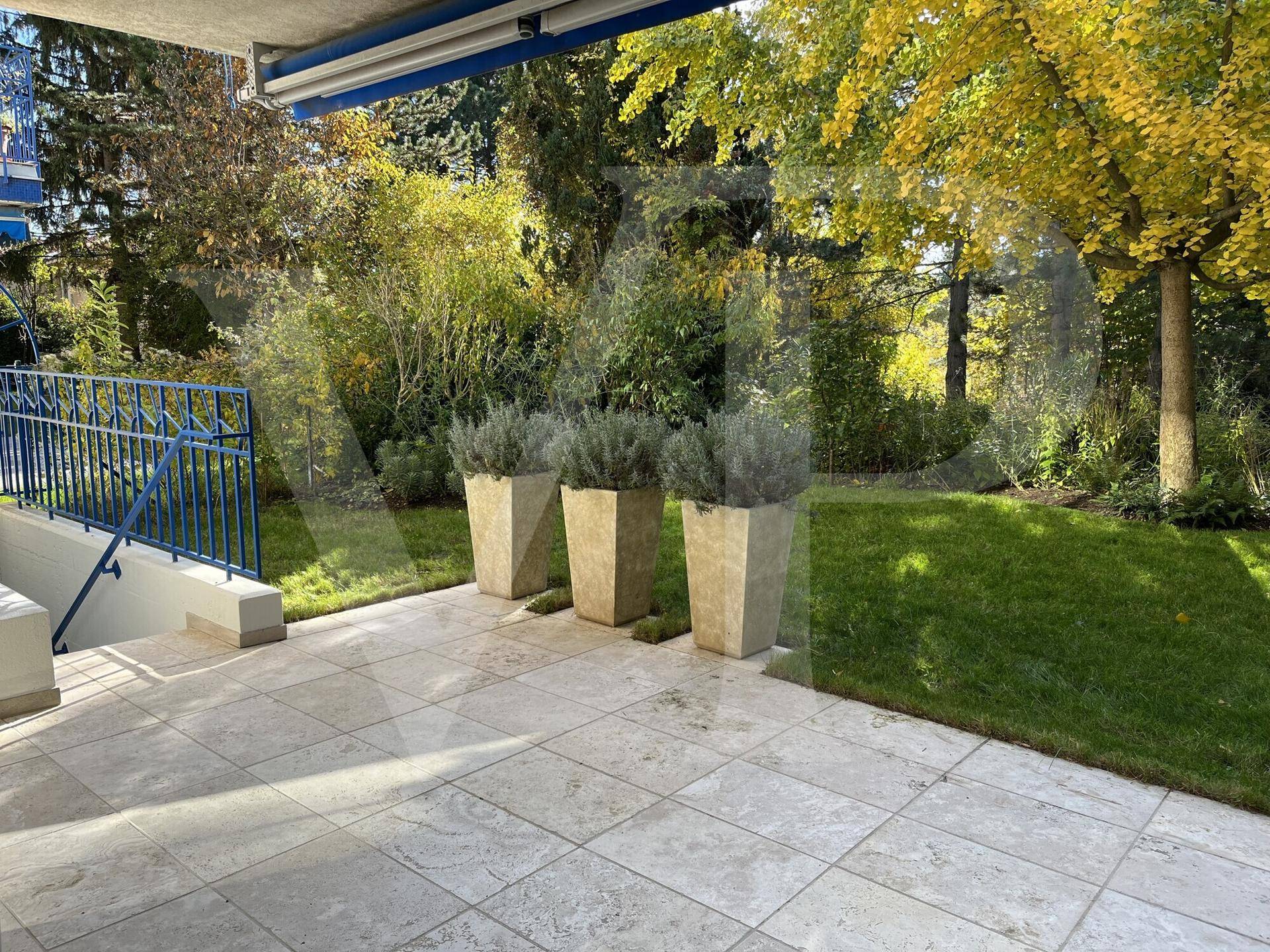 Sonnige Terrasse mit Fliesenboden, großen Pflanzkübeln und Blick auf den grünen Garten.