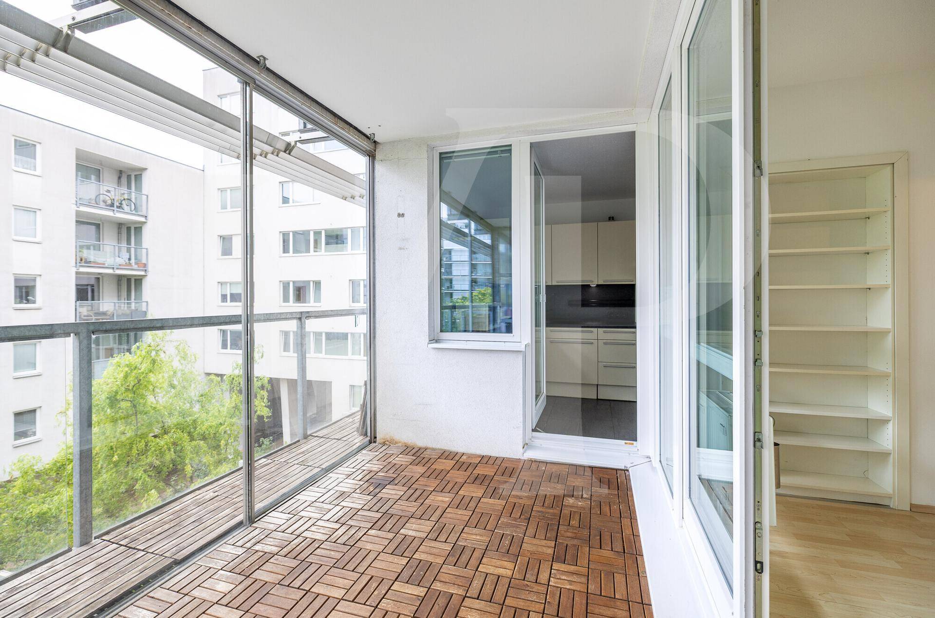 Verglaste Loggia mit Holzboden und Zugang zur Küche, bietet einen hellen Außenbereich.
