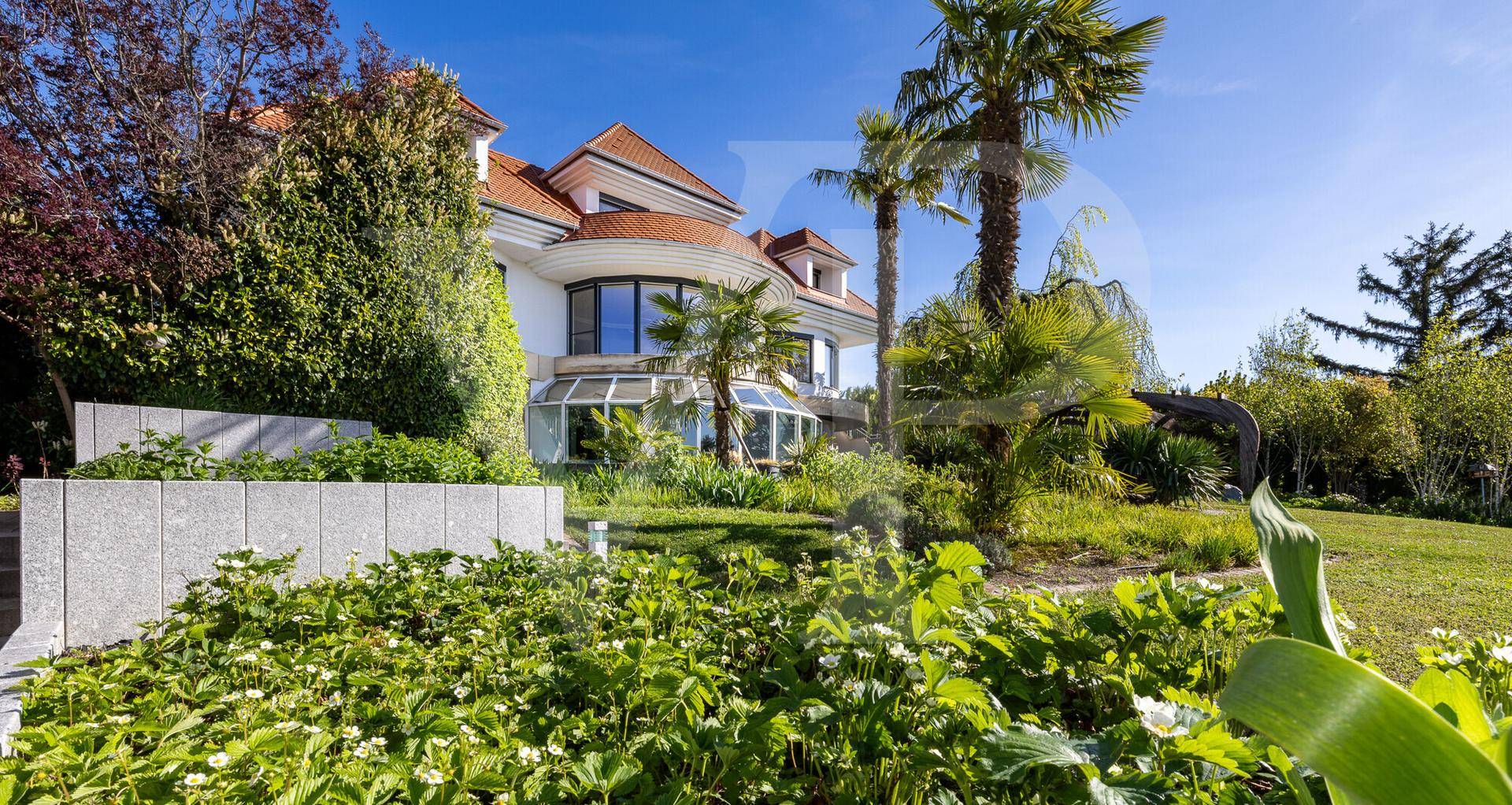 Elegante Villa umgeben von einem gepflegten Garten mit Palmen und Steinmauern.
