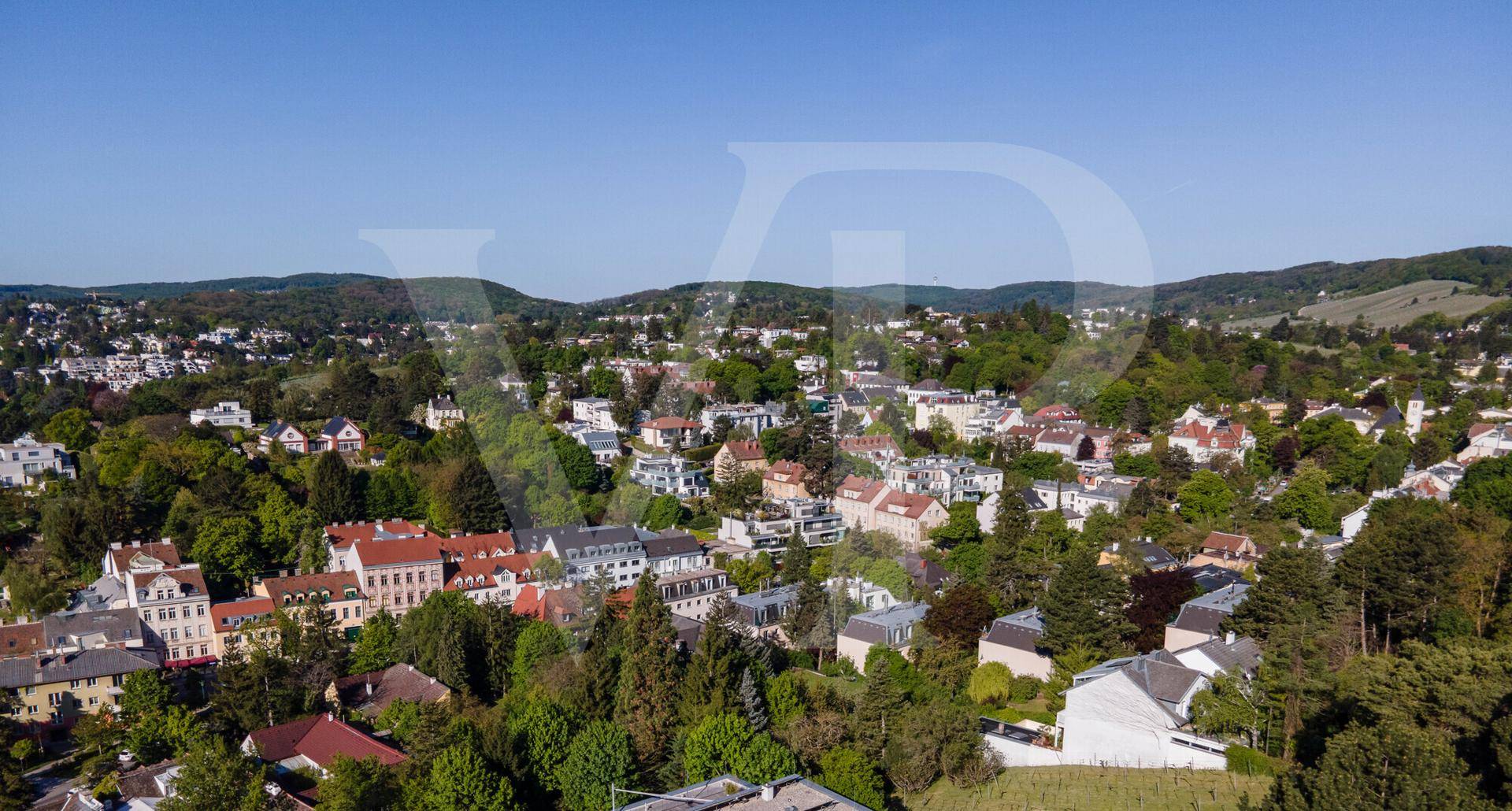 Ausblick auf eine hügelige Wohngegend mit vielen Häusern und üppiger Vegetation.
