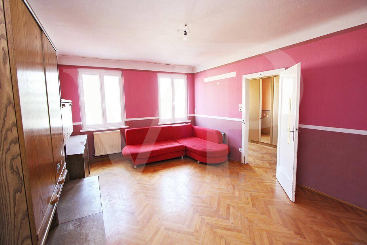 Wohnzimmer mit rosa Wänden, Fischgrätparkett und einem roten Ecksofa.