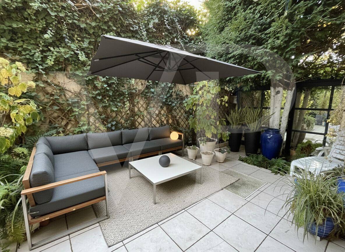 Möblierte Terrasse mit großem Sonnenschirm, bequemer Sitzecke und üppiger grüner Bepflanzung.