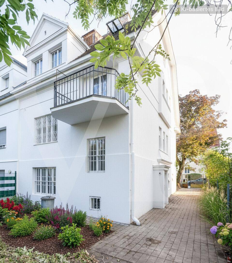 Seitenansicht des weißen Gebäudes mit kleinem Balkon, gepflastertem Weg und Blumenbeeten.