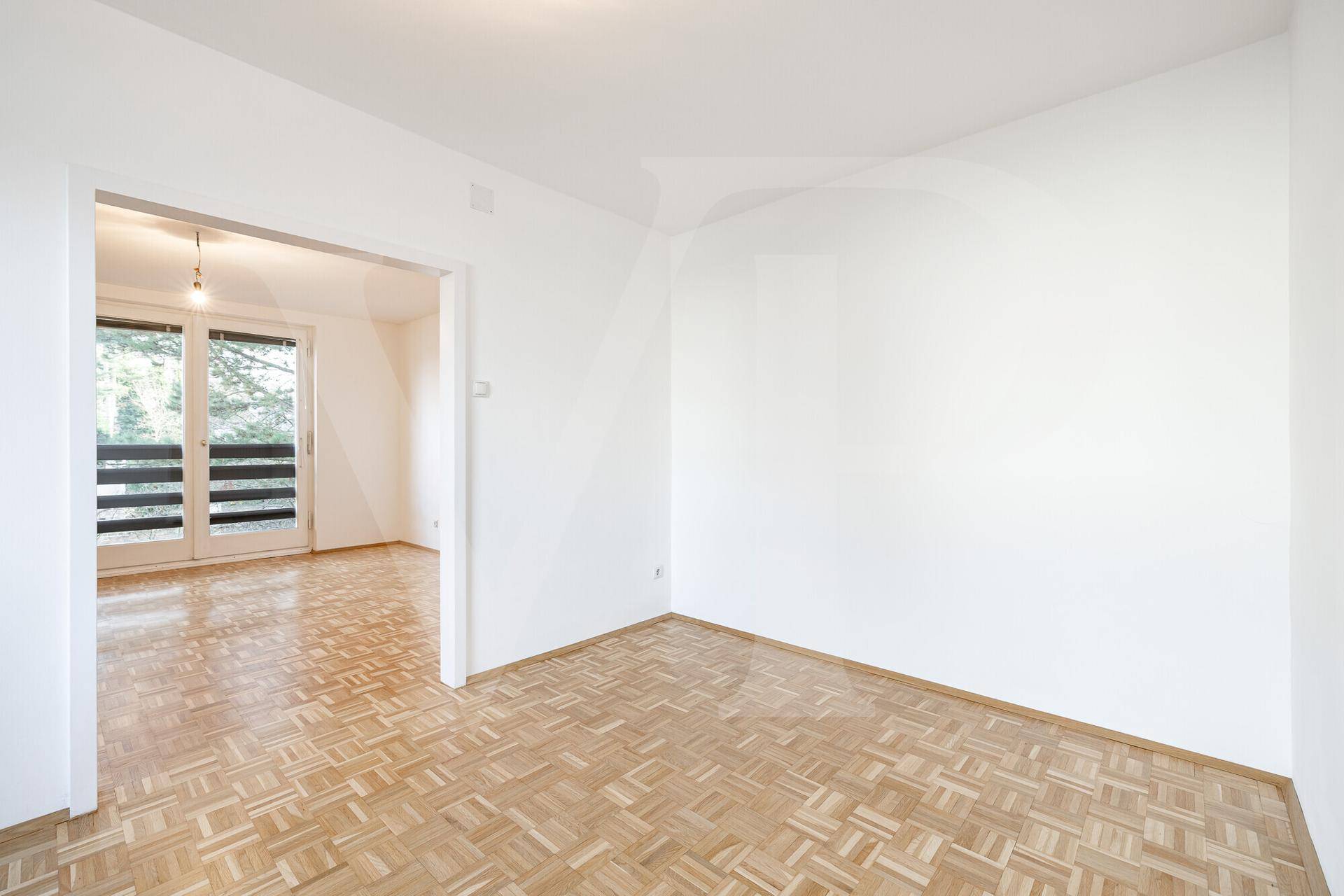 Helles Zimmer mit Parkettboden und offenem Übergang zu einem weiteren Wohnbereich.