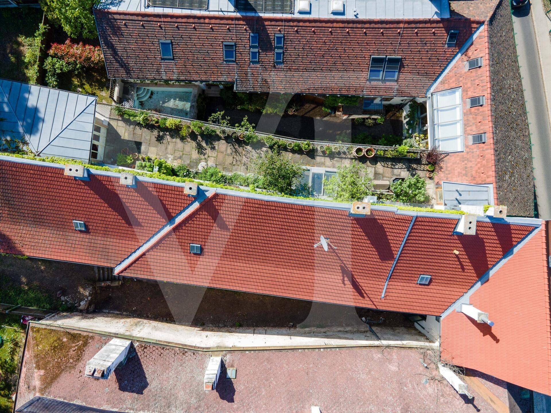 Vogelperspektive auf rote Ziegeldächer und einen begrünten Innenhof mit Poolbereich.