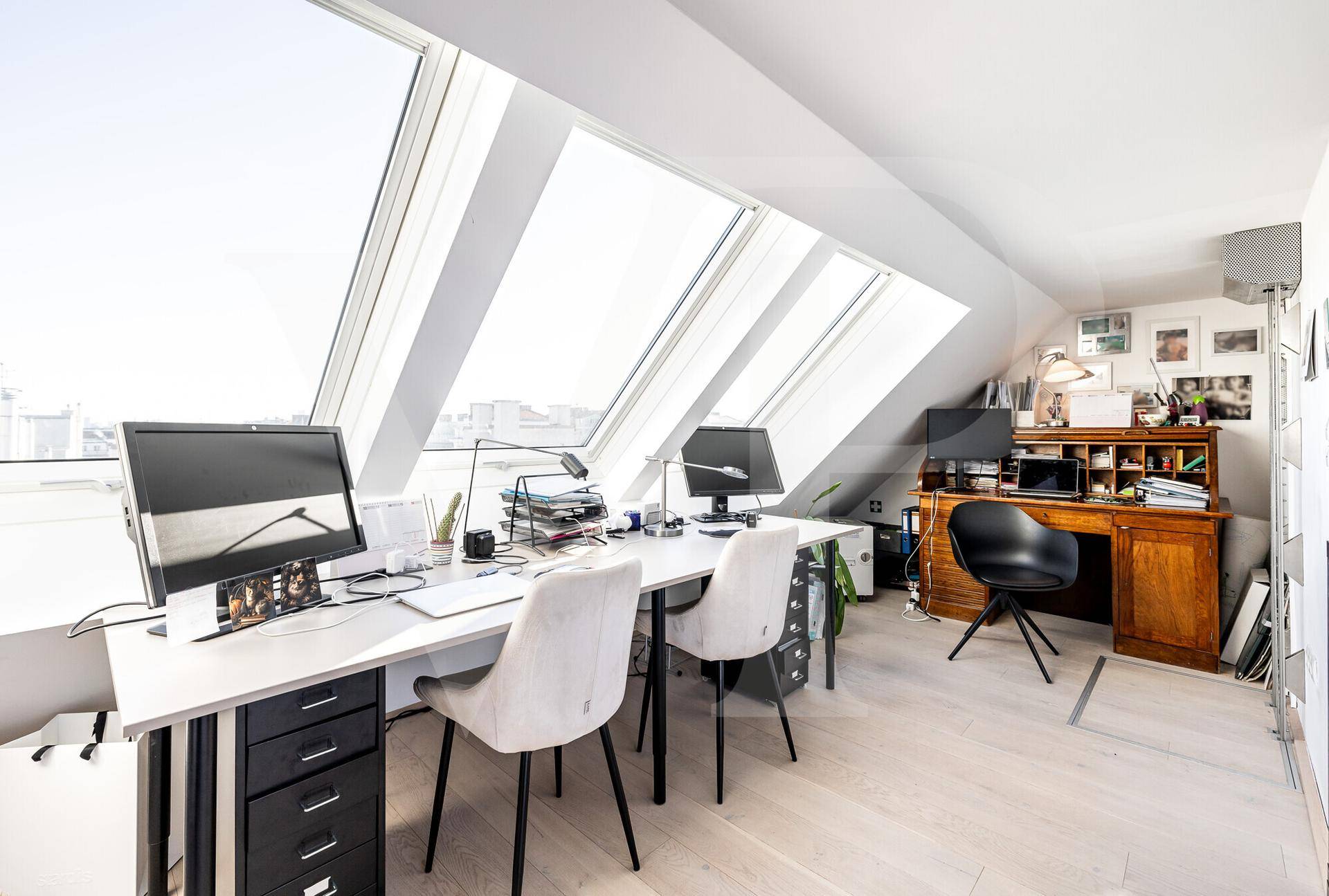 Helles Arbeitszimmer mit Dachfenstern, Holzboden und Blick über die Stadt.
