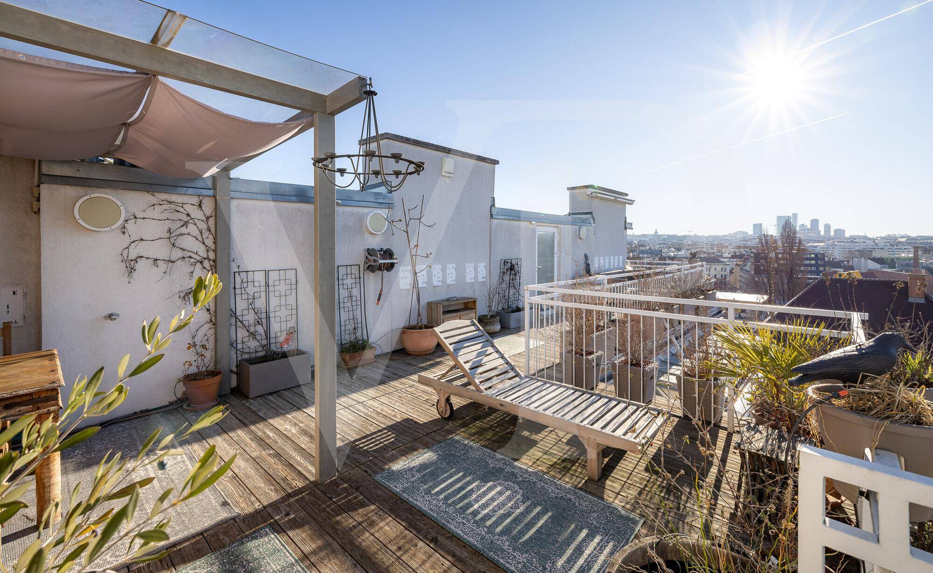 Sonnige Dachterrasse mit Holzdeck, Liegestuhl und weitem Blick auf die Stadt. Ideal zum Entspannen.
