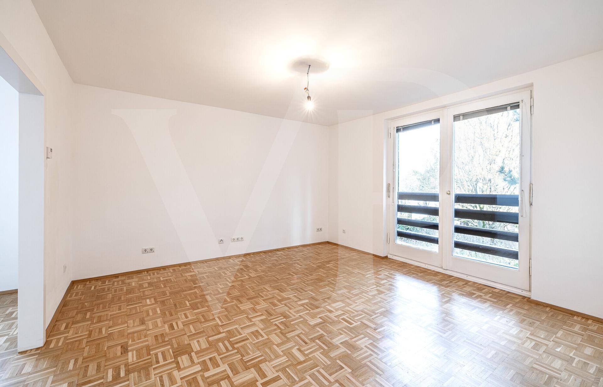 Heller Wohnraum mit Parkettboden und großen Fenstertüren, die auf einen Balkon führen.