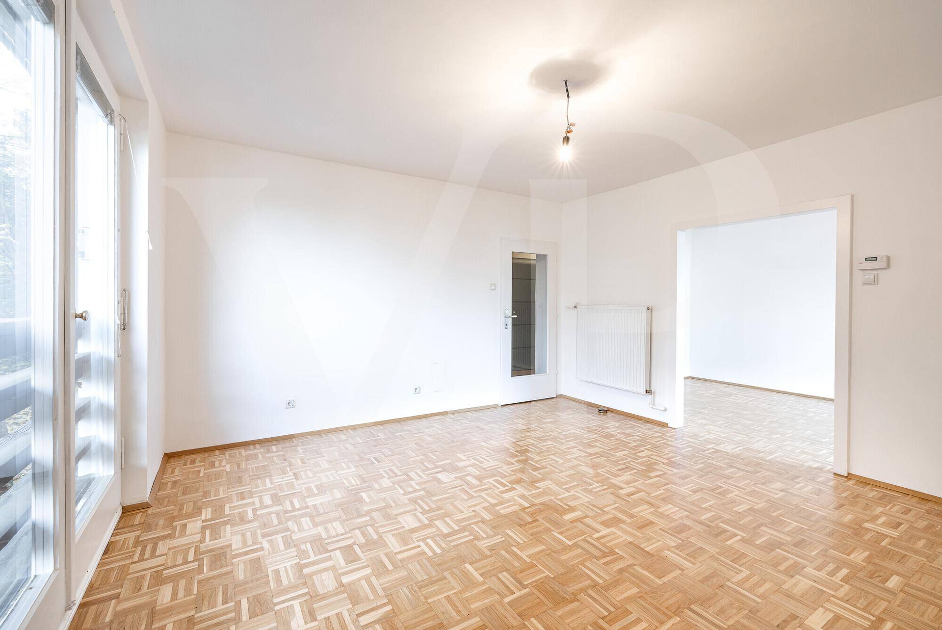 Geräumiger Wohnraum mit Parkettboden, weißen Wänden und direktem Zugang ins Freie.