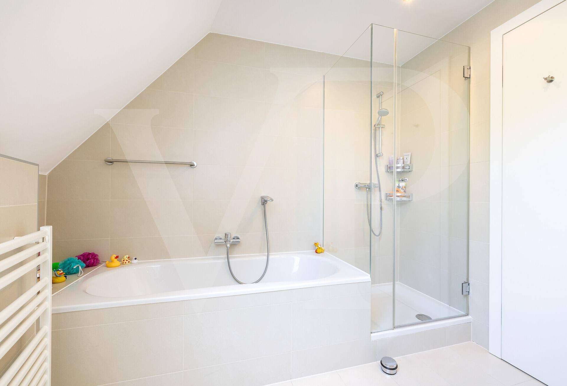 Helles Badezimmer mit Badewanne, Glasdusche und beheiztem Handtuchhalter unter einer Dachschräge.