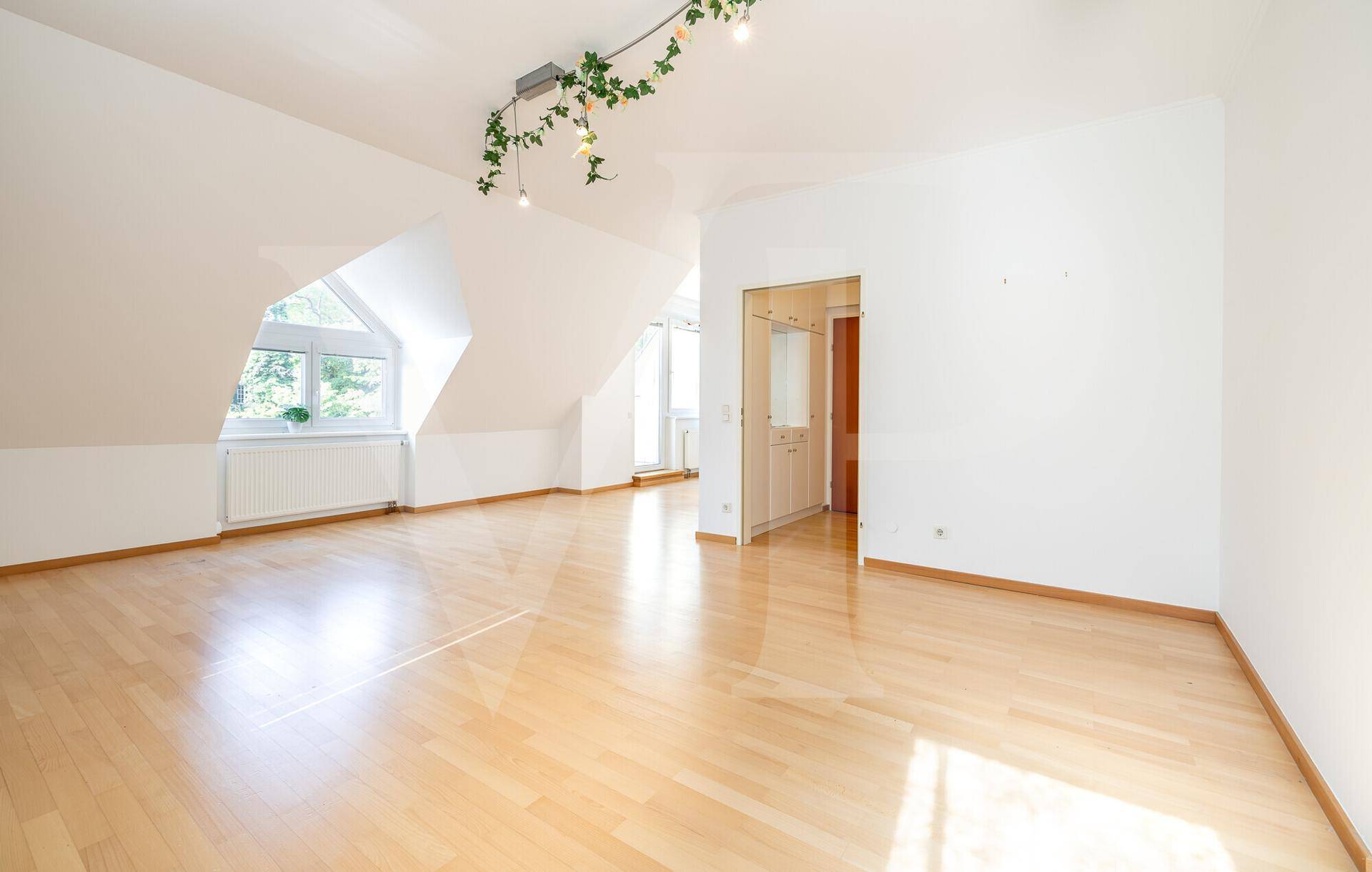 Heller Raum im Dachgeschoss mit schrägen Wänden, Holzfußboden und einem Fenster für viel Tageslicht.