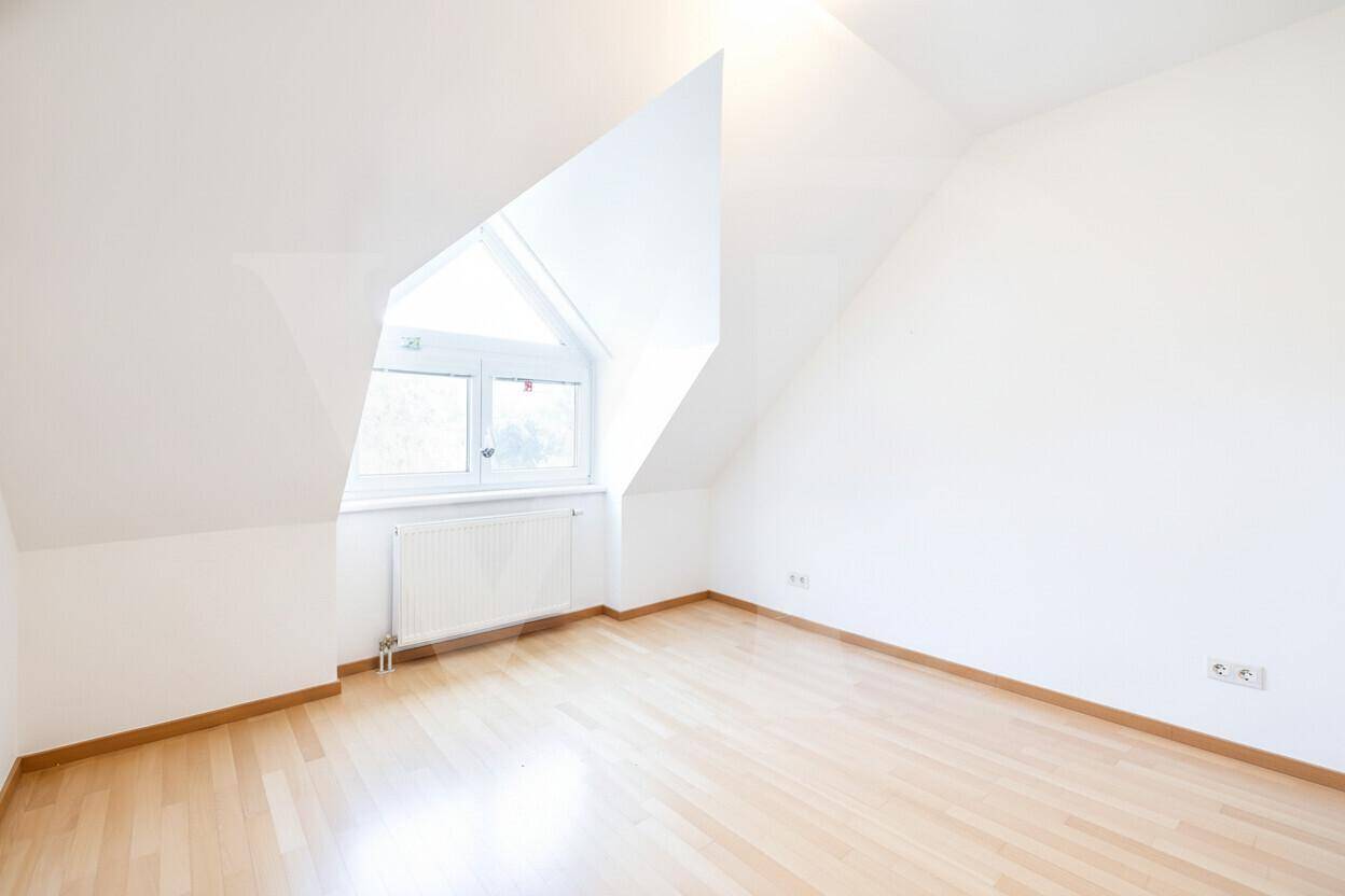 Leerer Raum im Dachgeschoss mit hellem Holzfußboden, schrägen Wänden und einem Fenster.