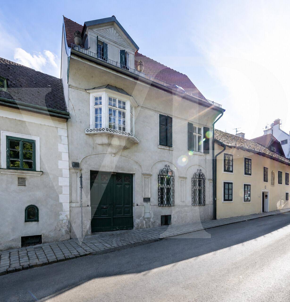 Historisches Gebäude mit Erkerfenster, grünen Fensterläden und Mansarddach an einer ruhigen Straße.