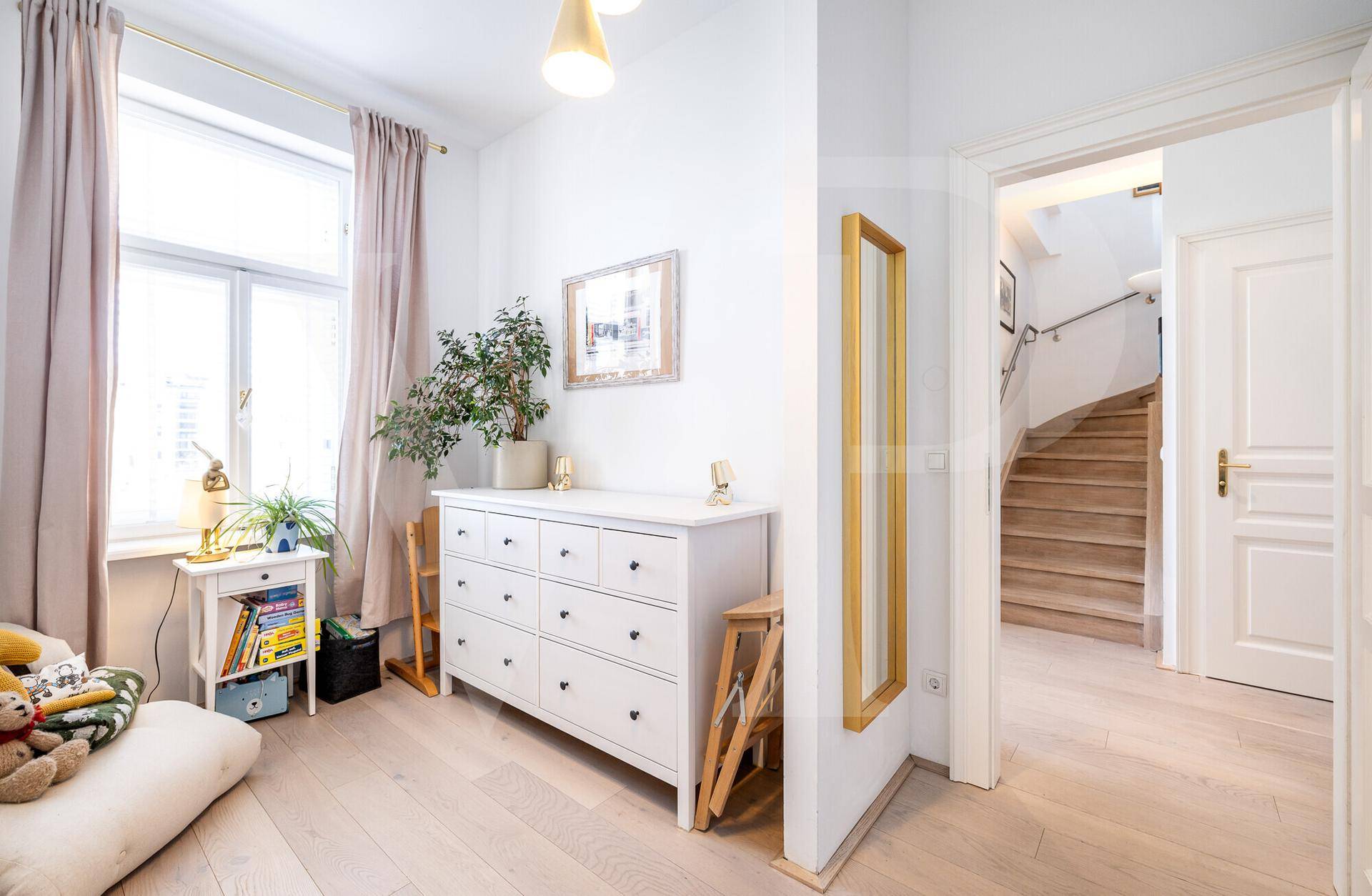 Helles Zimmer mit Kommode, Holzboden und Zugang zum Treppenhaus.
