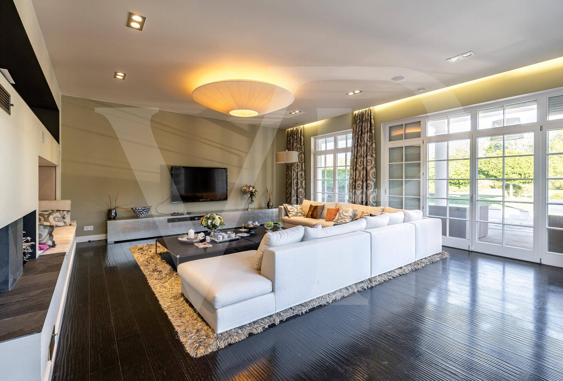 Geräumiges Wohnzimmer mit dunklem Holzboden, großer Couch und Zugang zur Terrasse.