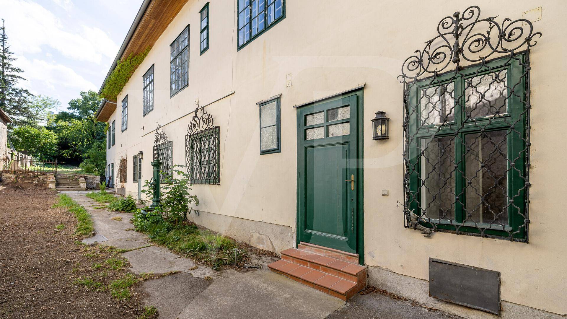 Historische Fassade mit grüner Eingangstür, verzierten Fenstern und einem gepflasterten Weg.