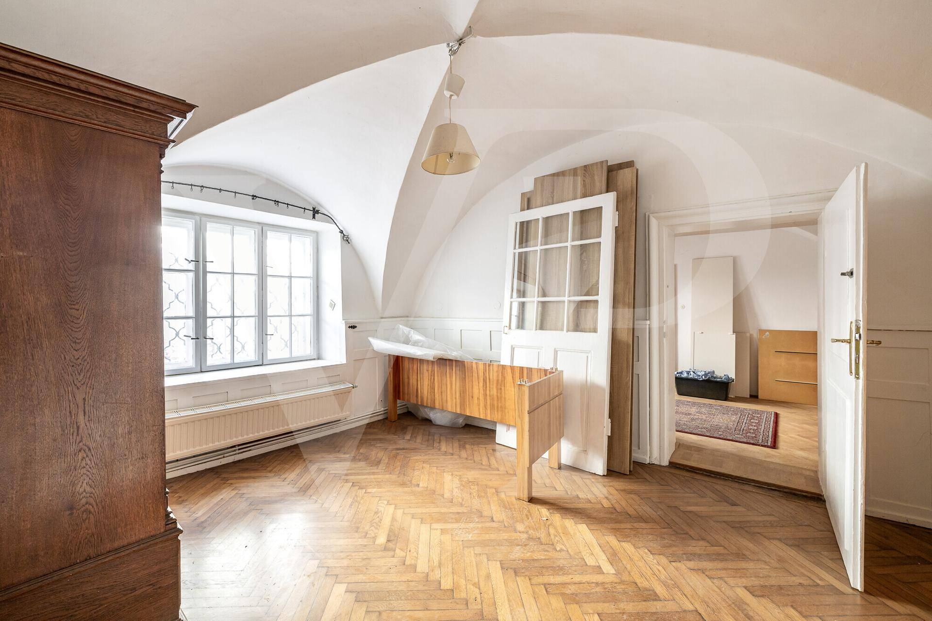 Geräumiges Zimmer mit beeindruckendem Gewölbedecke, Fischgrätparkett und großen Fenstern.