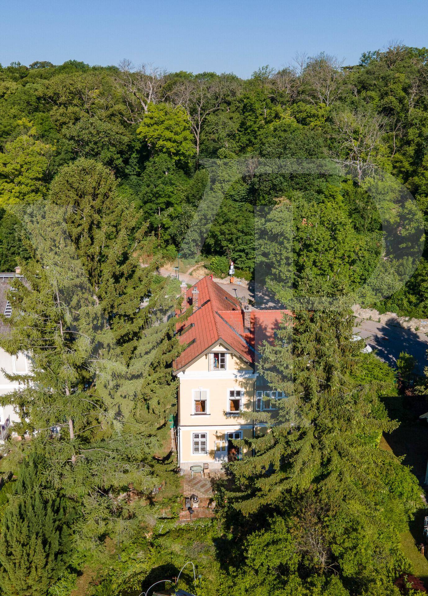 Historisches Gebäude mit rotem Dach, eingebettet in eine grüne Hügellandschaft.