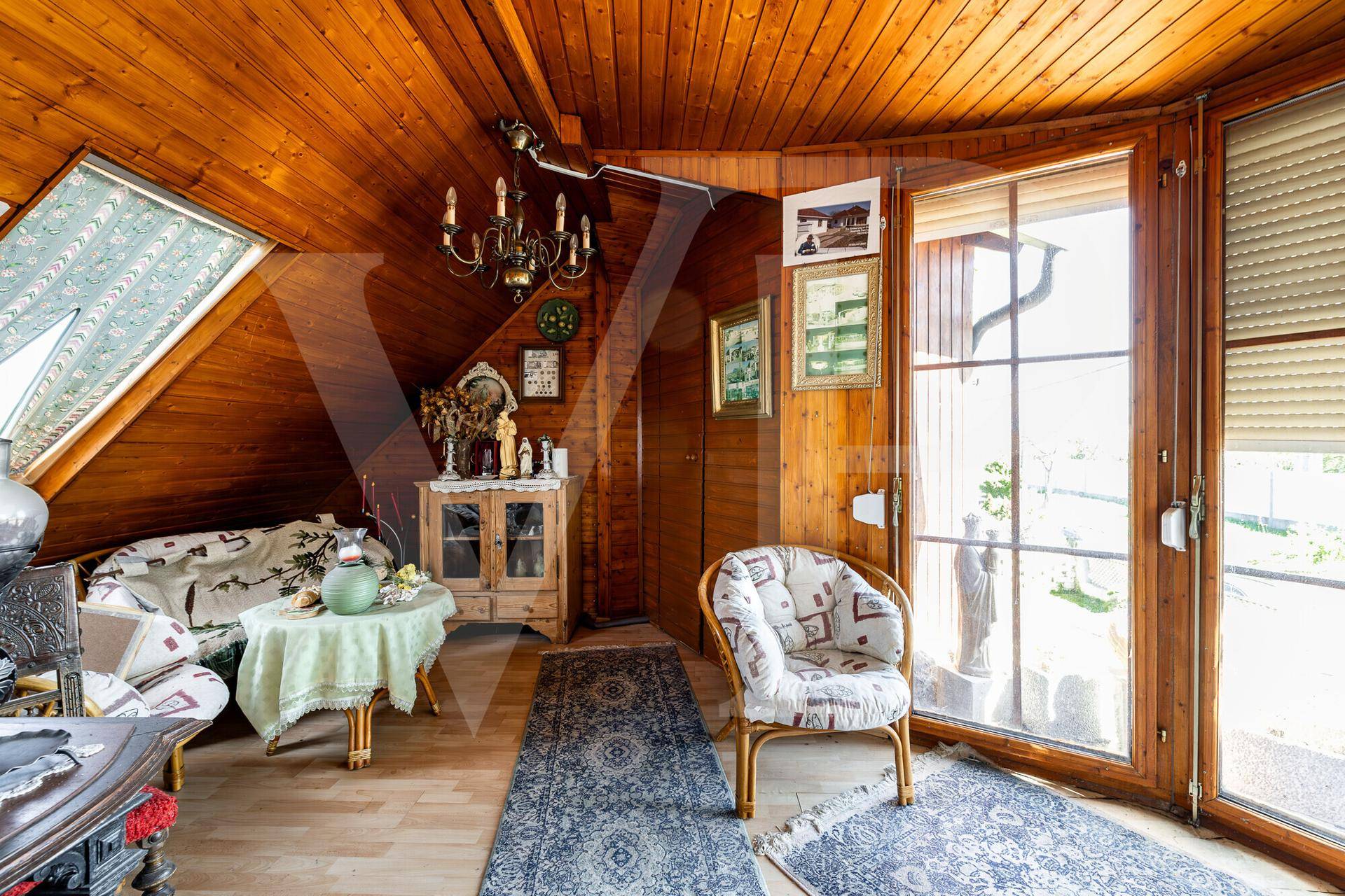 Gemütliches Wohnzimmer im Dachgeschoss mit Holzverkleidung, großen Fenstern und rustikalen Möbeln.