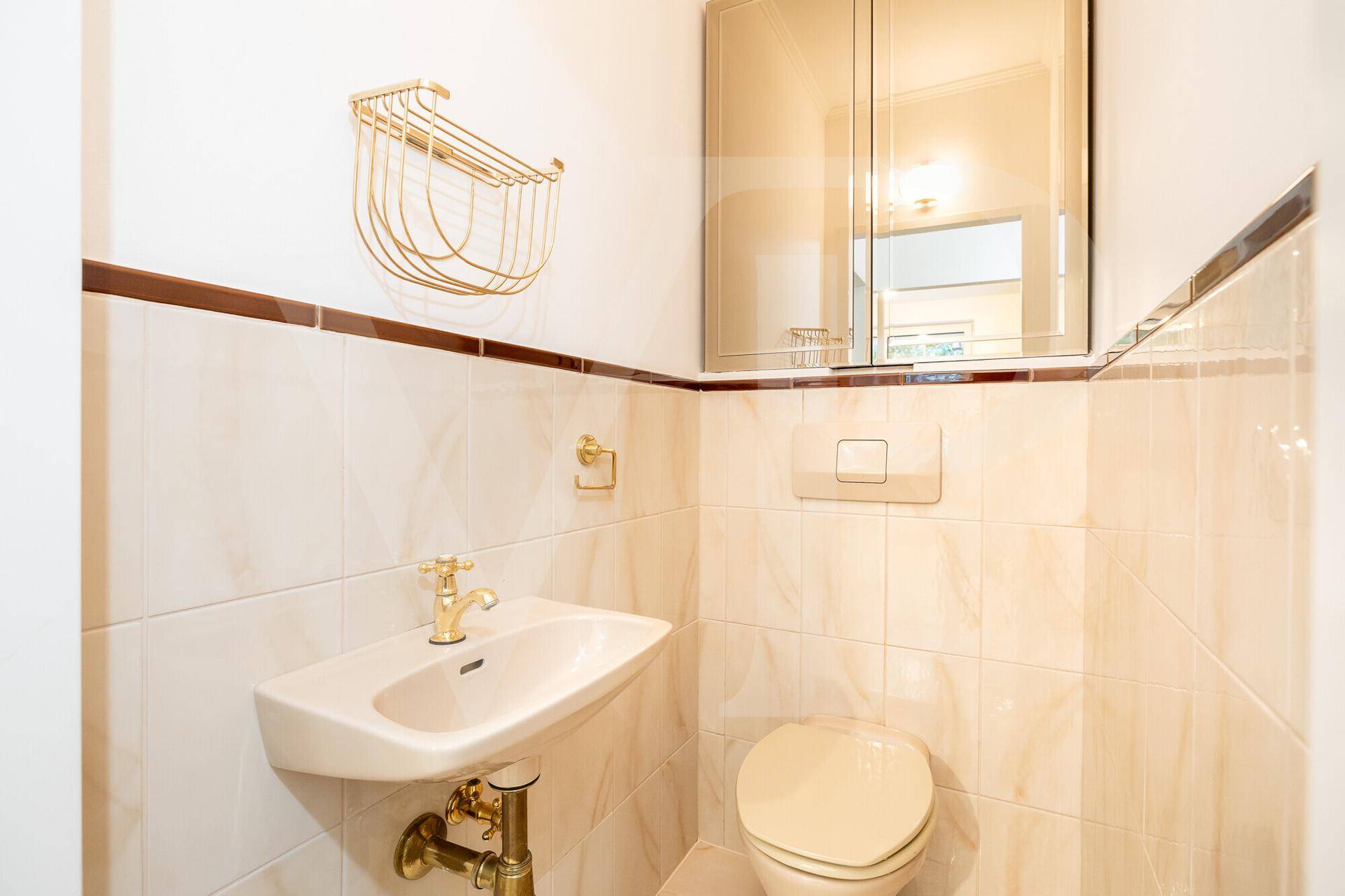 Kleines Gäste-WC mit beigefarbenen Fliesen, wandhängendem WC und Einzelwaschbecken.