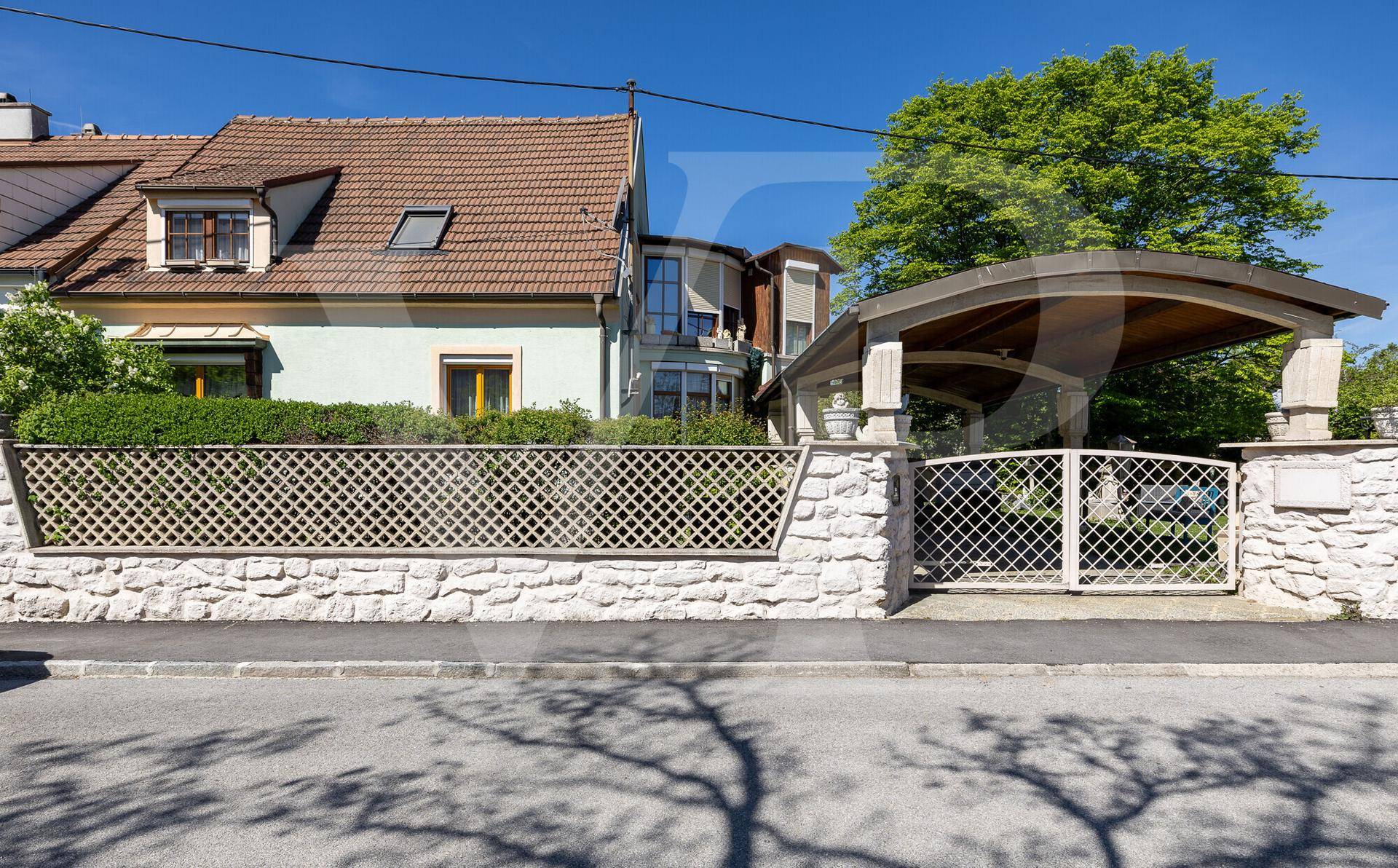Ansicht der Hausfassade von der Straße mit Carport und Steinmauer als Grundstücksbegrenzung.