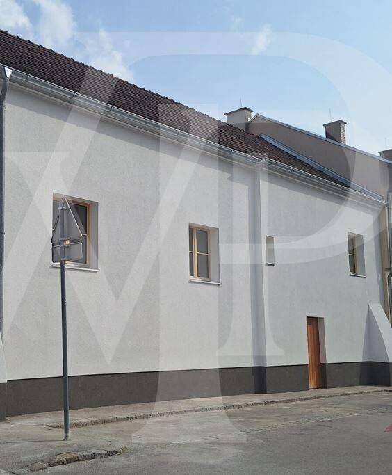 Schlichte weiße Fassade eines Gebäudes mit kleinen Fenstern und dunklem Sockel.