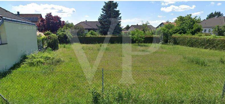 Unbebautes, grünes Baugrundstück mit hohem Gras und umgebenden Häusern in ruhiger Lage.