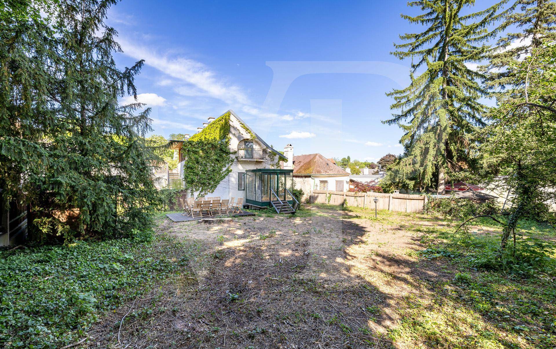 Großer, naturbelassener Garten mit altem Baumbestand und einem historischen Haus im Hintergrund.