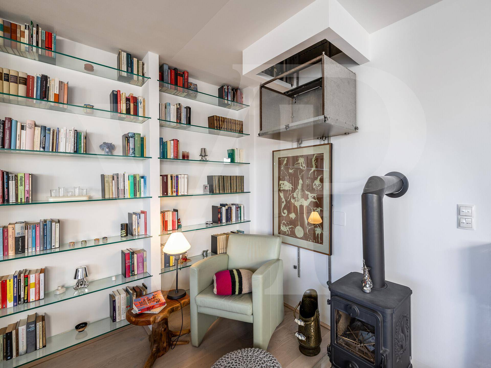 Gemütliche Leseecke mit Bücherregalen, Sessel und einem traditionellen Holzofen.