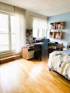 Schlafzimmer mit Holzboden, Schreibtisch und großen Fenstern, die viel Licht hereinlassen.