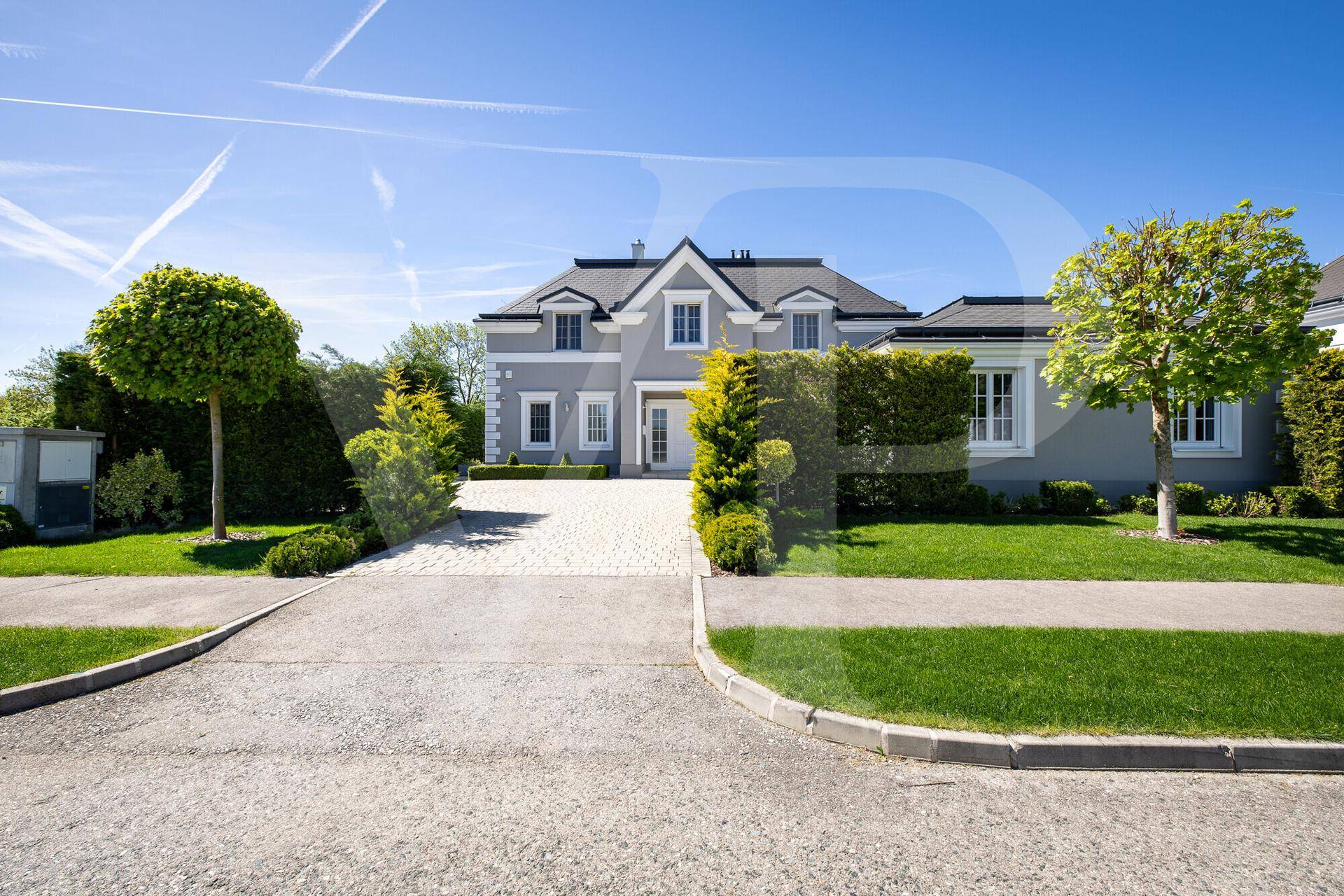 Elegante Villa mit gepflasterter Auffahrt und gepflegtem Vorgarten unter blauem Himmel.