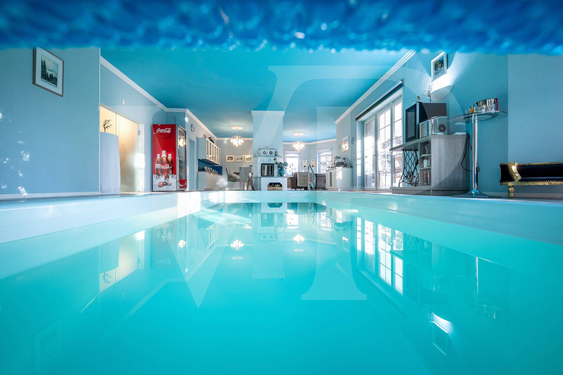 Blick aus dem Pool auf den großzügigen Wellnessbereich mit blauer Decke.