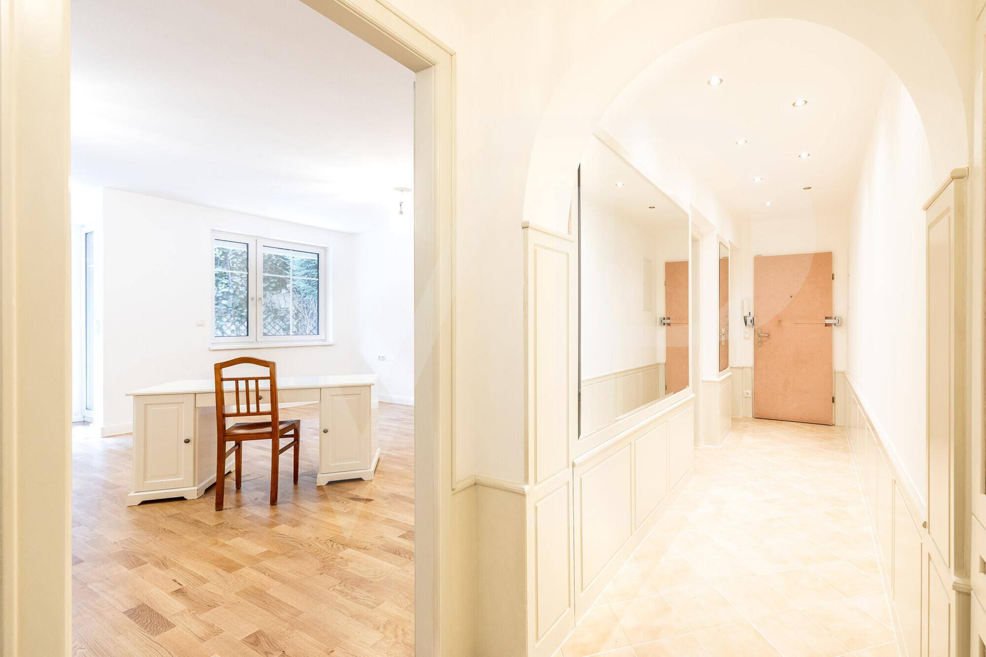 Heller Flur mit Holzboden und Spiegelflächen, der zu einem weiteren Zimmer mit Schreibtisch führt.