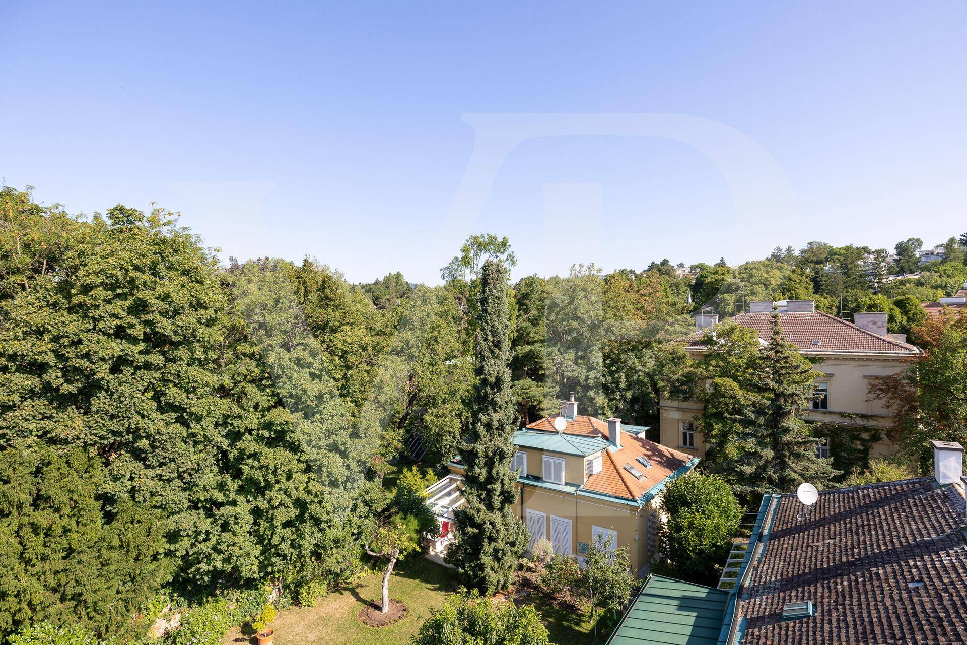 Panoramablick auf eine grüne Wohngegend mit Häusern und üppiger Vegetation unter blauem Himmel.