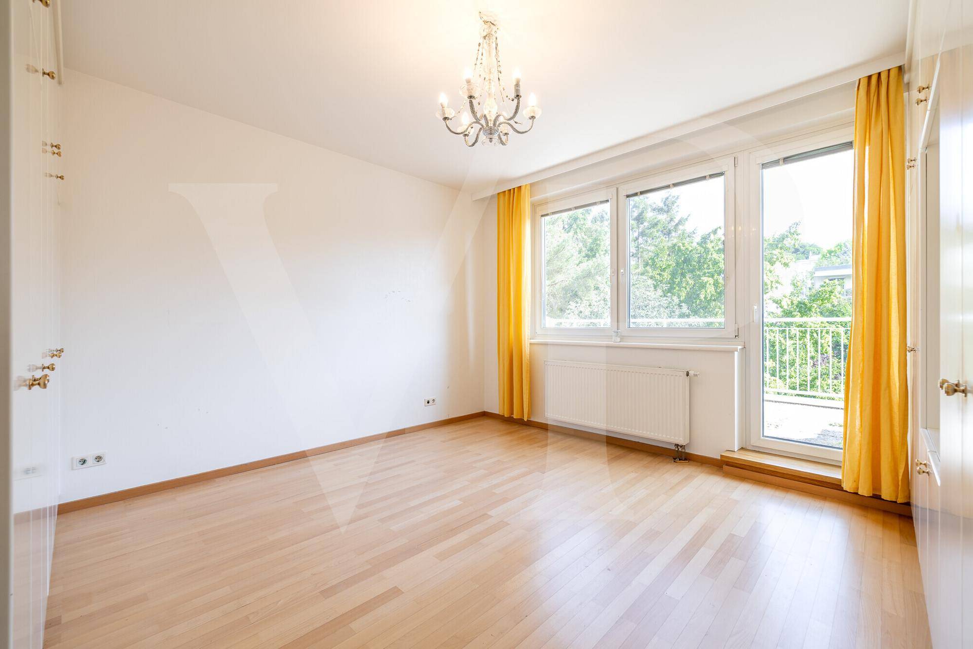 Heller Raum mit Holzfußboden, Kronleuchter und Zugang zu einem Balkon, bereit zur individuellen Gestaltung.